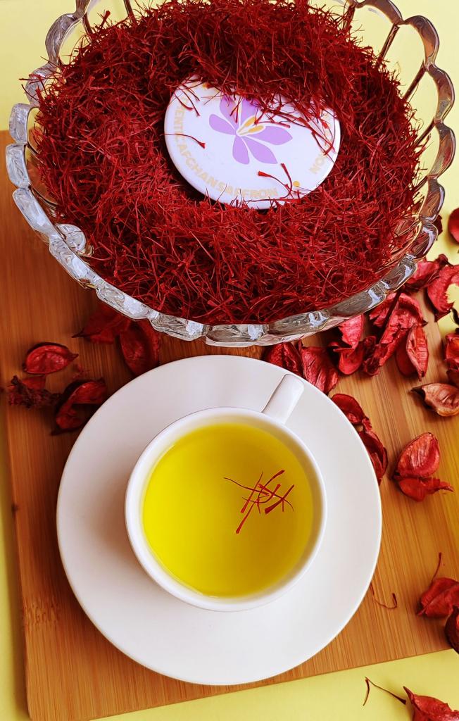 Overhead view of a white cup of golden Afghan saffron tea with red saffron threads floating on the surface