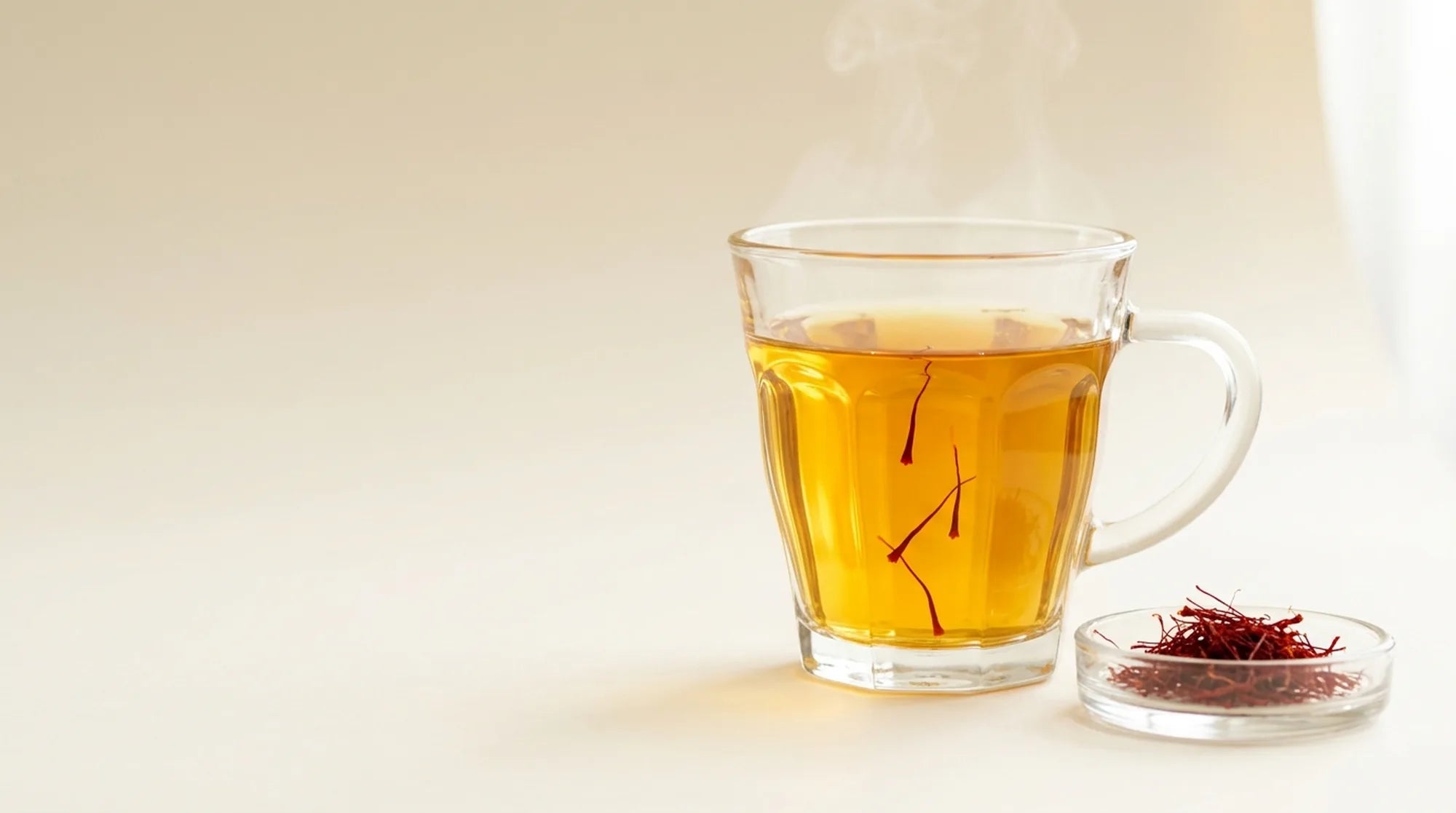 A crystal bowl of saffron threads beside a branded teacup of saffron tea bloomed deep gold