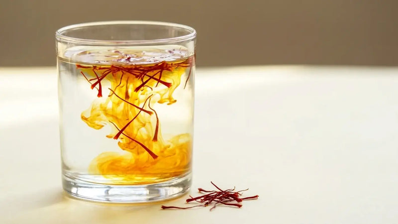 Saffron threads releasing a deep gold crocin plume through a clear glass of water, the ISO 3632 colour test