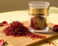 The Authentic Afghan Saffron crystal jar beside a heaped mound of all-red Super Negin threads and dried petals on a bamboo board