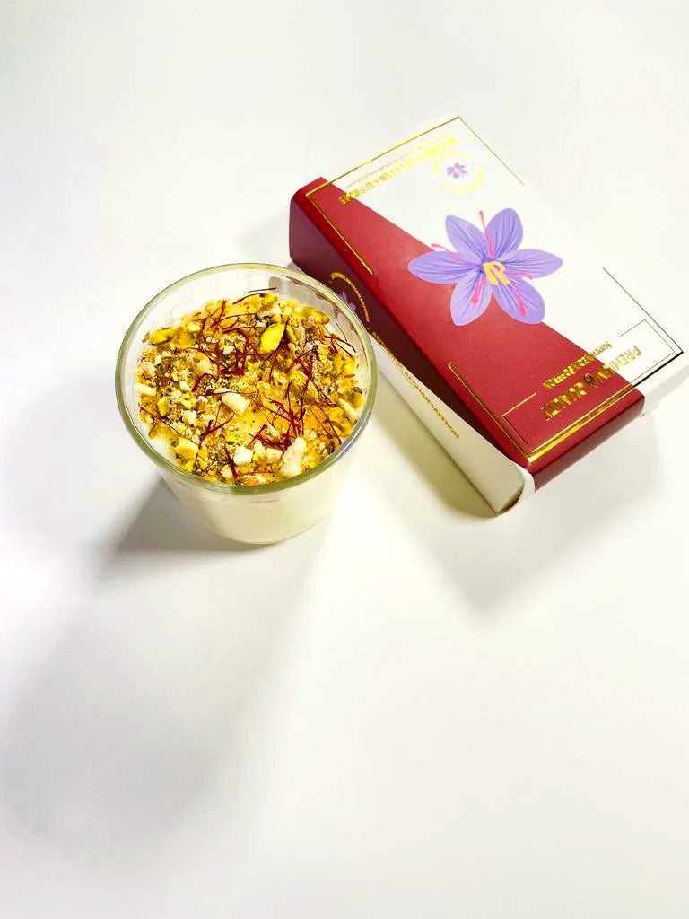 A glass teapot and branded teacup of golden Afghan saffron tea on a bamboo board against a saffron-yellow backdrop